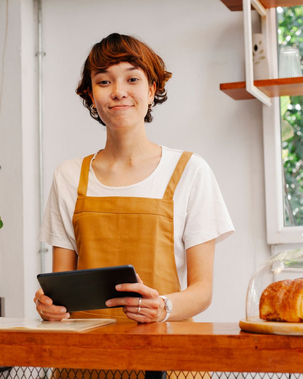 Illustrative photo: a smiling person at a bakery counter, holding a tablet